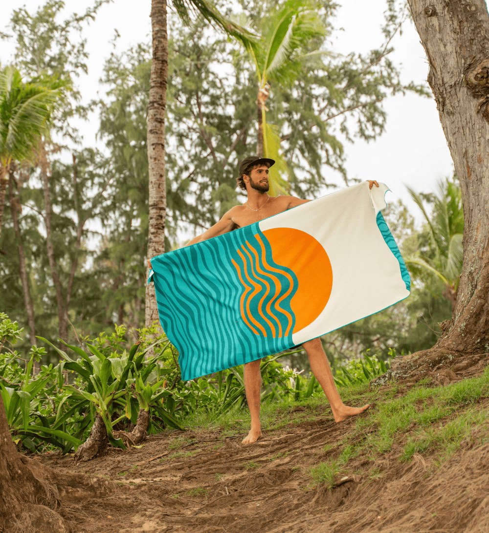 Man houdt een Buvanha reishanddoek Bora Bora met zon en golven open tussen palmbomen Man houdt een Buvanha reishanddoek Bora Bora met zon en golven open tussen palmbomen